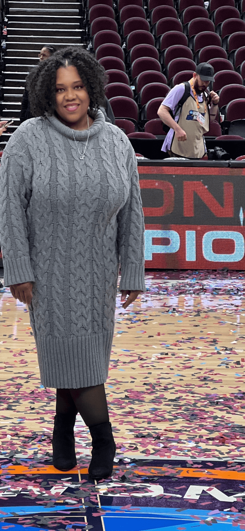 Karintha is wearing a grey sweaterdress while standing on the 2024 Women's Final Four Logo after the NCAA Championship game at Rocket Arena in Cleveland, OH